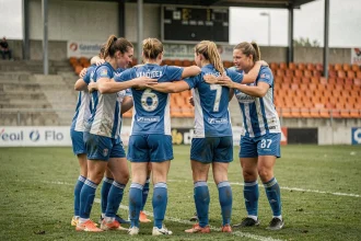 Joueuses de football féminin en cercle sur un terrain en herbe naturelle dans le district de Vendée, portant des maillots bleu et blanc